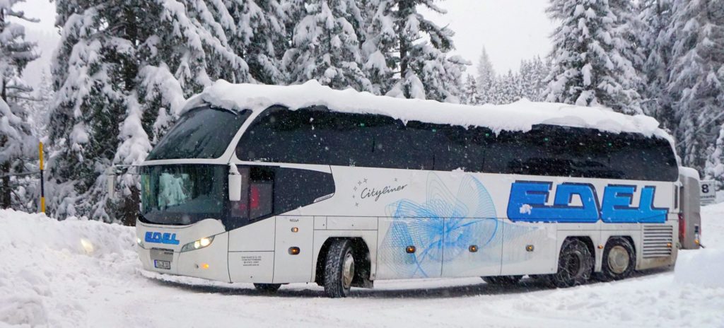 Winter-Reisen mit Edel Reisen, Rottenburg am Neckar. Der Reisebus blinkt und startet gerade mitten im Schnee. Die Winterreise im Bus geht weiter